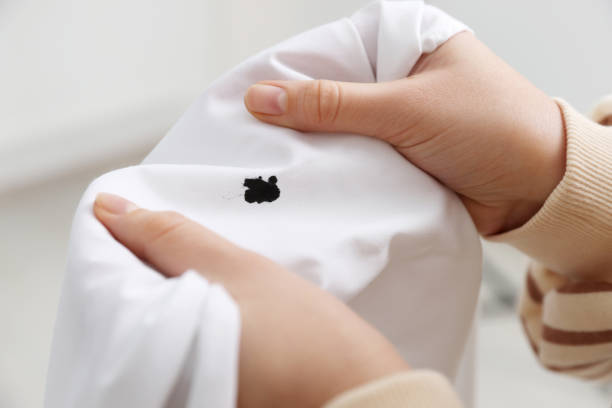 Hands attempting to remove a black ink stain from a white piece of clothing.